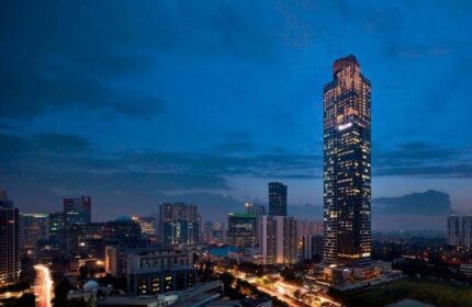 Night view of The Westin Jakarta, a gay-friendly hotel. The Jakarta skyline features illuminated skyscrapers against a dark blue sky.