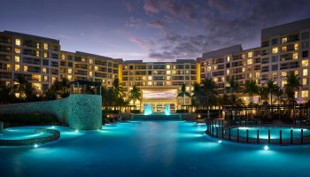 The Westin Lagunamar Ocean Resort Villas & Spa Cancun at dusk. Gay-friendly hotel with illuminated pools and palm trees. A luxury travel destination.