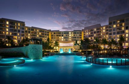 The Westin Lagunamar Ocean Resort Villas & Spa Cancun at dusk. Gay-friendly hotel with illuminated pools and palm trees. A luxury travel destination.