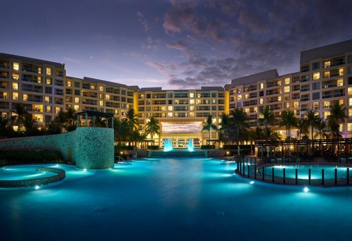 The Westin Lagunamar Ocean Resort Villas & Spa Cancun at dusk. Gay-friendly hotel with illuminated pools and palm trees. A luxury travel destination.