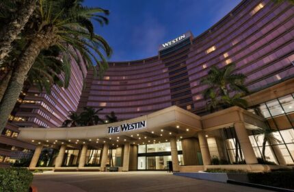 The Westin Long Beach hotel exterior at dusk. Gay-friendly hotel with palm trees. Entrance to The Westin is lit up.