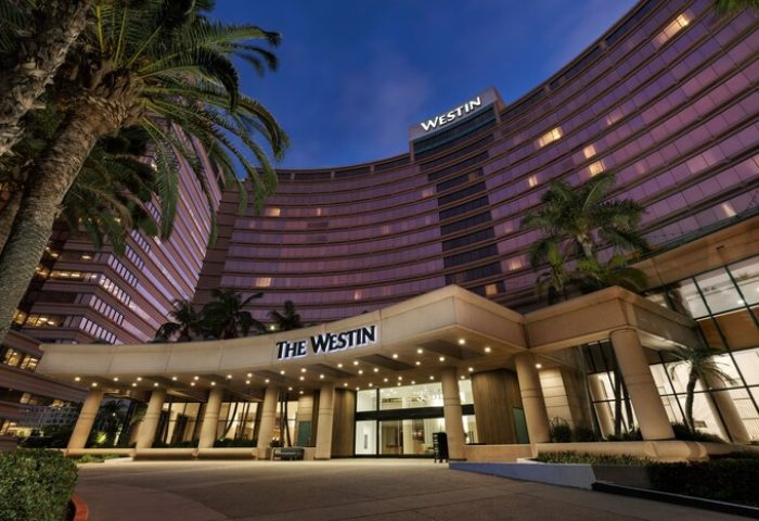 The Westin Long Beach hotel exterior at dusk. Gay-friendly hotel with palm trees. Entrance to The Westin is lit up.