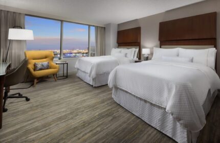 The Westin Long Beach hotel room with two beds, a yellow chair, and a view of the city. Gay-friendly hotel room.