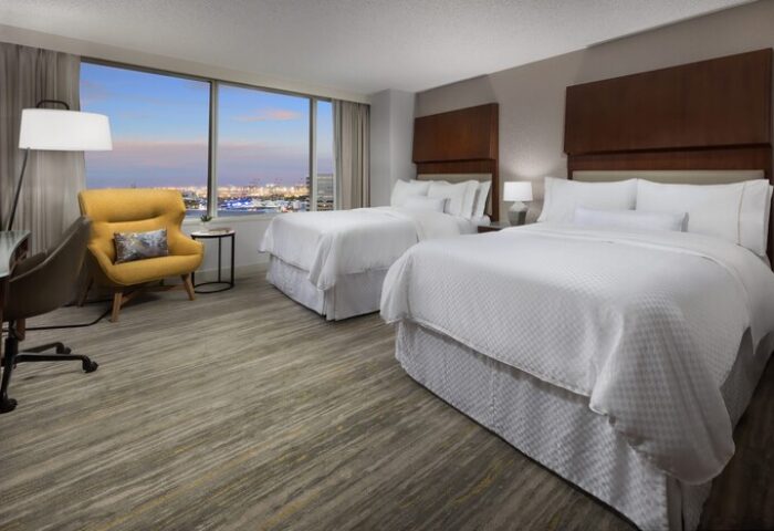 The Westin Long Beach hotel room with two beds, a yellow chair, and a view of the city. Gay-friendly hotel room.