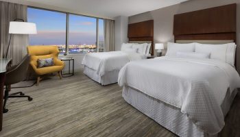 The Westin Long Beach hotel room with two beds, a yellow chair, and a view of the city. Gay-friendly hotel room.