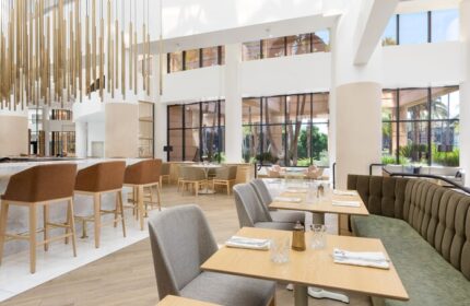 The Westin Long Beach gay-friendly hotel restaurant. Interior view with tables, chairs, bar stools, and large windows. Modern design.