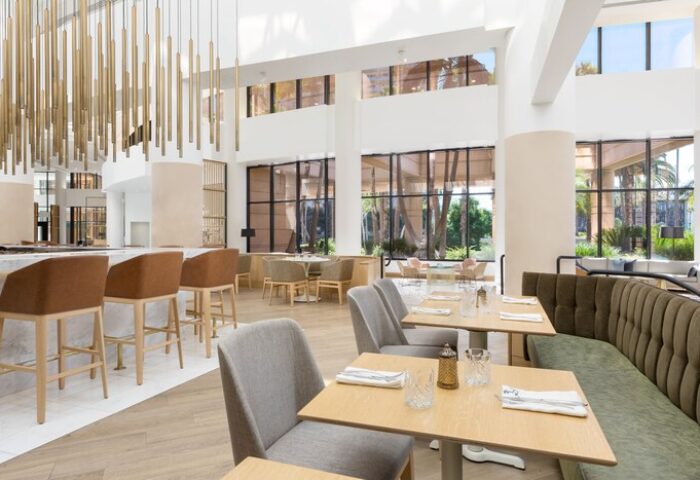 The Westin Long Beach gay-friendly hotel restaurant. Interior view with tables, chairs, bar stools, and large windows. Modern design.