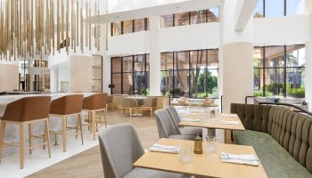 The Westin Long Beach gay-friendly hotel restaurant. Interior view with tables, chairs, bar stools, and large windows. Modern design.