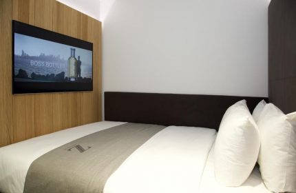 The Z Hotel City room. Gay-friendly hotel with bed, pillows, and TV showing Boss Bottled ad. Modern design for gay travelers.