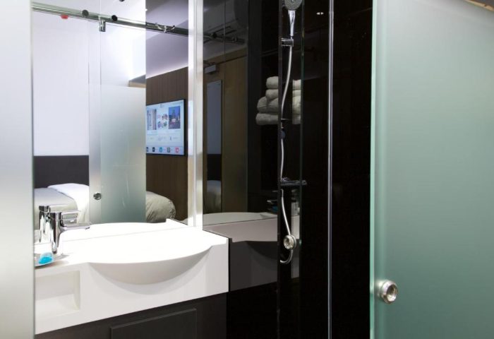 Bathroom at The Z Hotel City, a gay-friendly hotel. Features a modern sink, shower, and a view into the bedroom with a TV. Ideal for gay travelers.