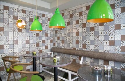 Interior of The Z Hotel Piccadilly, a gay-friendly hotel. Features tables, chairs, a bench, patterned walls, and green pendant lights.