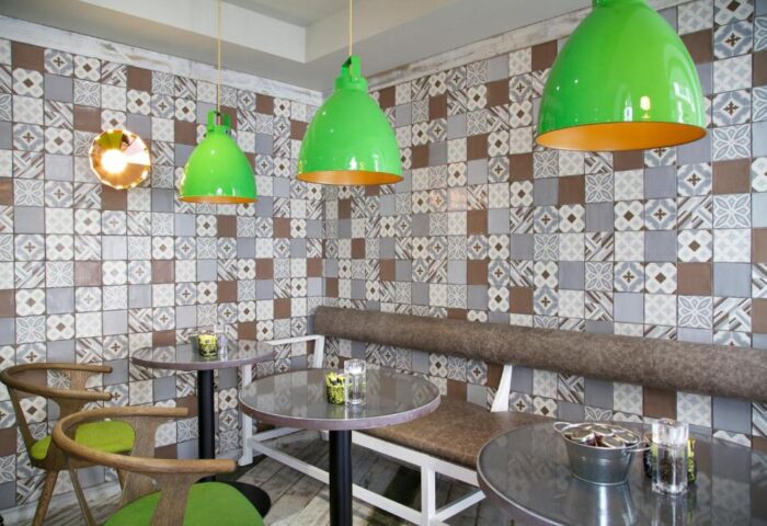 Interior of The Z Hotel Piccadilly, a gay-friendly hotel. Features tables, chairs, a bench, patterned walls, and green pendant lights.