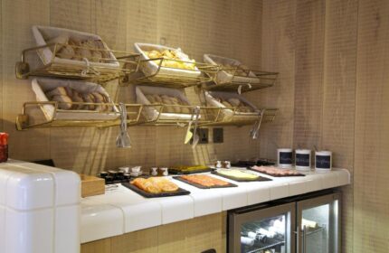 Breakfast buffet at The Z Hotel Soho, a gay-friendly hotel. Breads in baskets, cold cuts, cheese, and yogurt are displayed on a white tiled counter.