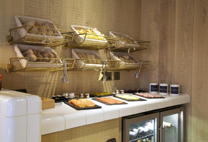 Breakfast buffet at The Z Hotel Soho, a gay-friendly hotel. Breads in baskets, cold cuts, cheese, and yogurt are displayed on a white tiled counter.