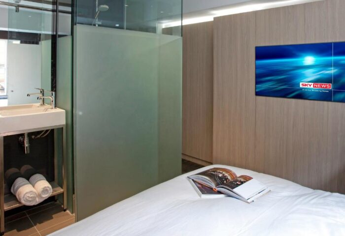 The Z Hotel Soho room: bed with a book, TV, and glass-enclosed bathroom. Modern design at this gay-friendly hotel in Soho, London.