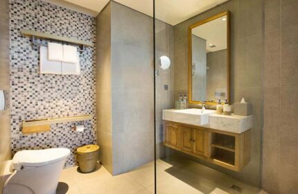 Tijili Hotel Seminyak bathroom. Modern design with mosaic tiles, wooden vanity, & large mirror. Gay-friendly hotel for discerning travelers.