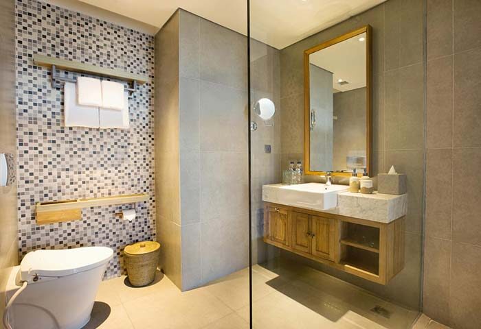 Tijili Hotel Seminyak bathroom. Modern design with mosaic tiles, wooden vanity, & large mirror. Gay-friendly hotel for discerning travelers.