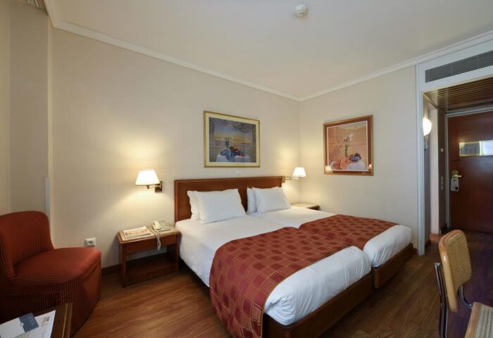 Gay-Friendly Titania Hotel room. Twin beds with red patterned covers, paintings, and a red chair. Comfortable stay for gay travelers.