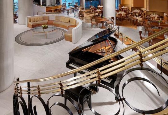 Titania Hotel's grand lobby with a piano, seen from the stairs. Gay-friendly hotel with elegant design and dining areas.