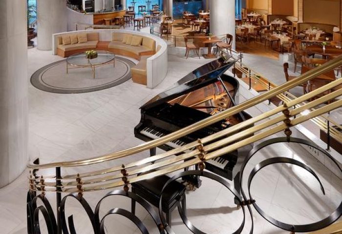 Titania Hotel's grand lobby with a piano, seen from the stairs. Gay-friendly hotel with elegant design and dining areas.