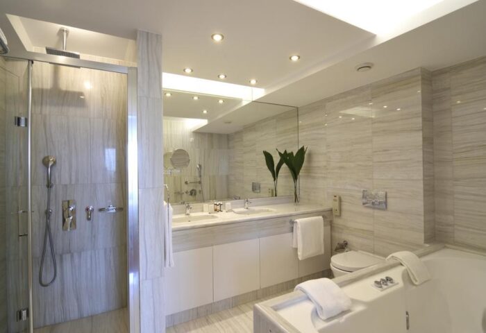 Titania Hotel gay-friendly bathroom. Features a marble shower, double sinks, a bathtub, and modern fixtures. Ideal for gay men travelers.