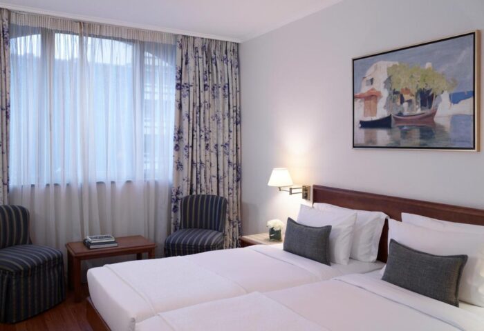 Titania Hotel gay-friendly double room. Interior view of the hotel room with twin beds, chairs, curtains, and painting.
