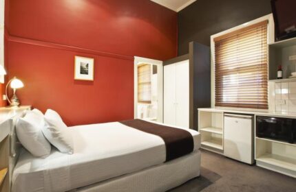 Tolarno Hotel room. Gay-friendly hotel with a bed, red wall, wardrobe, window with blinds, microwave, and mini-fridge. Gay travel advice.