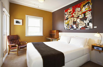Tolarno Hotel room: Queen bed with brown throw, colorful art, leather chair, desk, and window. Gay-friendly hotel room for gay men travel.