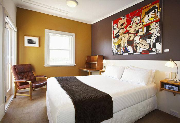 Tolarno Hotel room: Queen bed with brown throw, colorful art, leather chair, desk, and window. Gay-friendly hotel room for gay men travel.