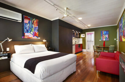 Tolarno Hotel gay-friendly room. Bedroom with king bed, kitchenette, red sofa, dining table, wood floors. Modern art. Gay travel.