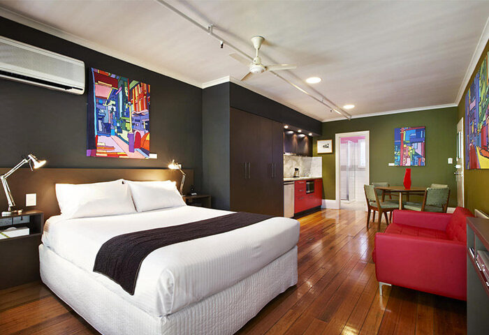 Tolarno Hotel gay-friendly room. Bedroom with king bed, kitchenette, red sofa, dining table, wood floors. Modern art. Gay travel.