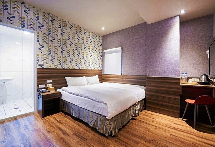 Tomorrow Hotel gay-friendly room. Double bed with white sheets, patterned wallpaper, wood-look flooring, and en-suite bathroom with shower.