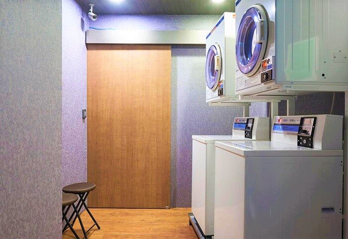 Laundry room at Tomorrow Hotel, a gay-friendly hotel. Two sets of stacked washers and dryers, a wooden door, and a stool.