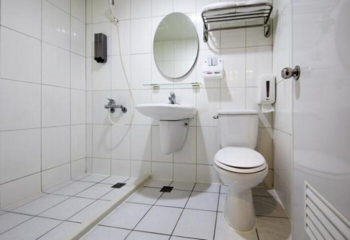 Tomorrow Hotel bathroom. Clean white tiled room with toilet, sink, shower, and mirror. Gay-friendly hotel bathroom.