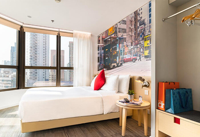 Travelodge Central Hollywood Road gay-friendly hotel room. City view, double bed, Hong Kong street scene mural, bags. Modern, clean design.
