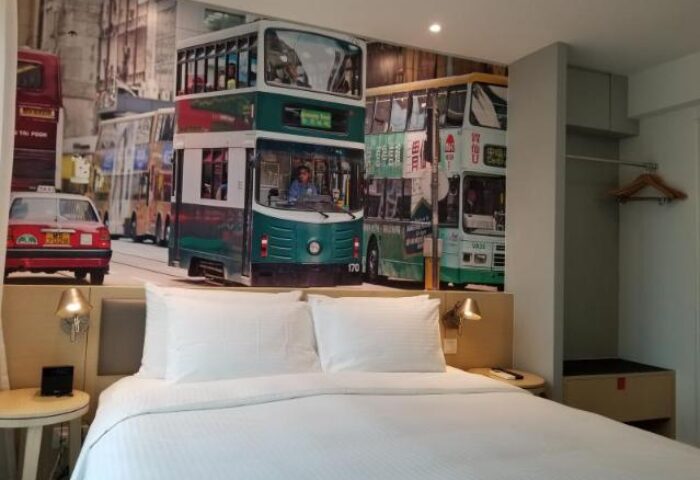 Travelodge Central Hollywood Road gay-friendly hotel room. Hong Kong bus and taxi mural above a bed with white linens.