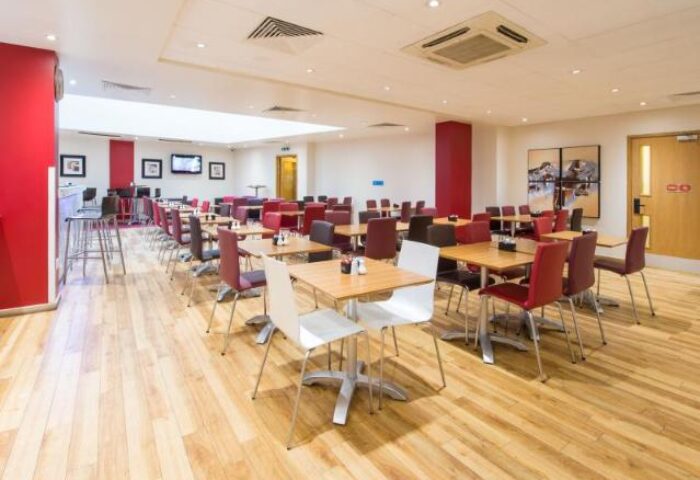 Travelodge London Central Southwark's dining area. Gay-friendly hotel with tables and chairs on a wood floor. Red and white decor.