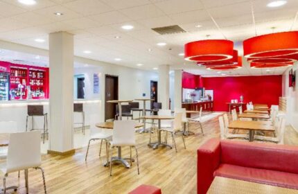 Travelodge London Vauxhall's bar and dining area. This gay-friendly, pet-friendly hotel features a modern design with red accents and wooden floors.