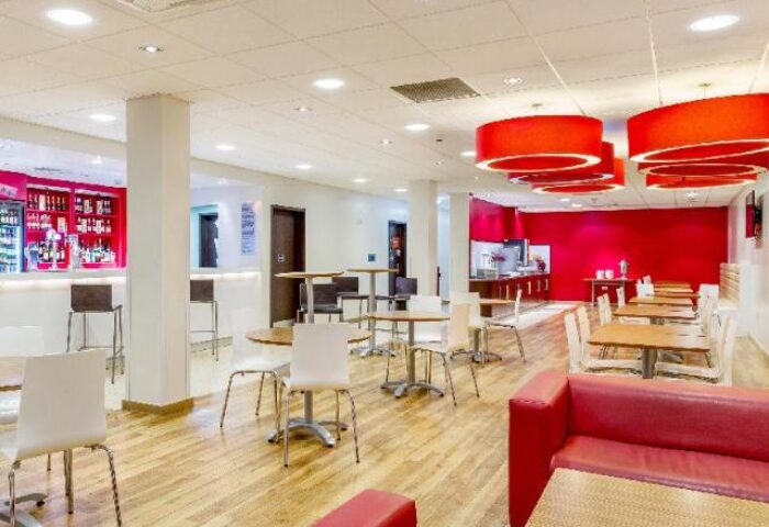 Travelodge London Vauxhall's bar and dining area. This gay-friendly, pet-friendly hotel features a modern design with red accents and wooden floors.