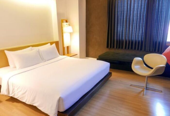 Trinity Silom Hotel gay-friendly room. King bed with white linens, modern chair, and window seat. A comfortable stay in Bangkok's gay district.