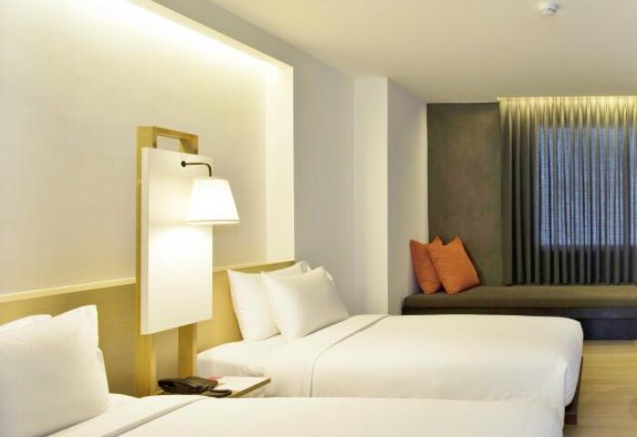 Gay-friendly Trinity Silom Hotel room with twin beds, white linens, and orange pillows. A comfortable stay in Bangkok's gay district.