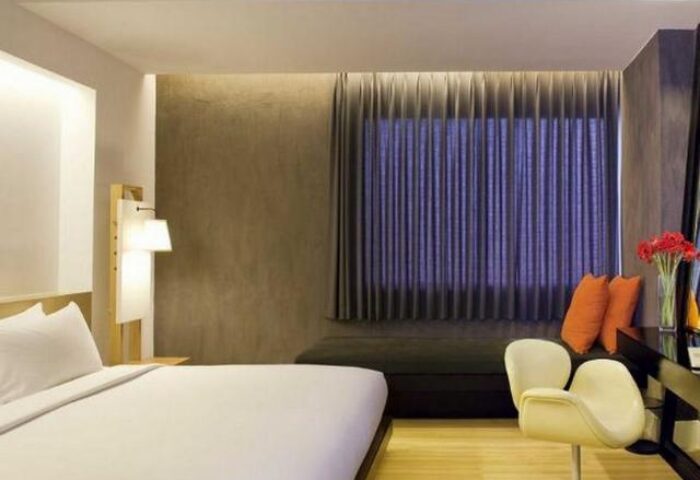 Trinity Silom Hotel room. Gay-friendly hotel in Bangkok. Modern design, bed, desk, chair, and window with curtains. Comfortable stay in Silom.