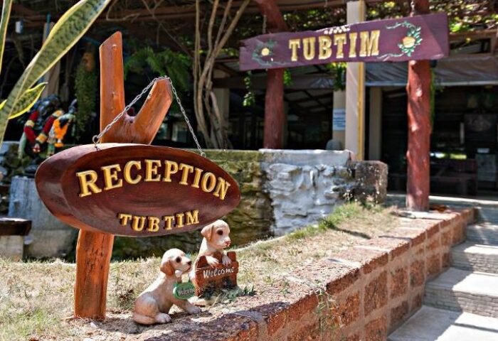 Reception sign at Gay-Friendly Hotel Tubtim Resort, a welcoming destination. Two puppy statues add charm to this tropical gay travel spot.
