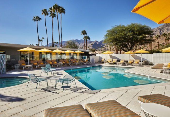 Twin Palms Resort, Palm Springs' gay men's getaway. Poolside loungers, yellow umbrellas, palm trees, and mountain views create a relaxing vibe.
