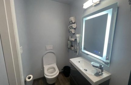 Bathroom at Gay-Friendly Twin Peaks Hotel. Modern design with toilet, sink, illuminated mirror, and gray walls. Gay travel accommodations.