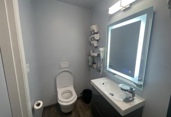 Bathroom at Gay-Friendly Twin Peaks Hotel. Modern design with toilet, sink, illuminated mirror, and gray walls. Gay travel accommodations.