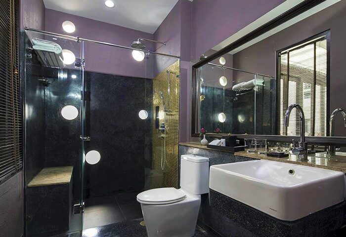 U Chiang Mai gay-friendly hotel bathroom. Shower with round windows, toilet, and sink. Modern design and purple walls. Luxury travel.