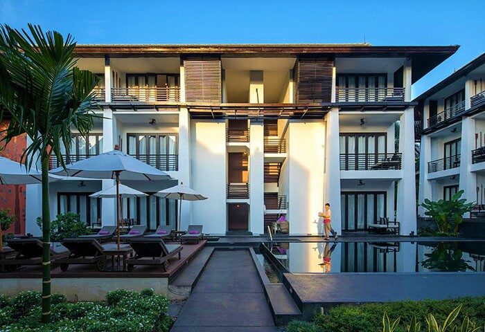 U Chiang Mai gay-friendly hotel's exterior. Poolside view with sunbeds, umbrellas, and a staff member. Ideal for gay men travel.