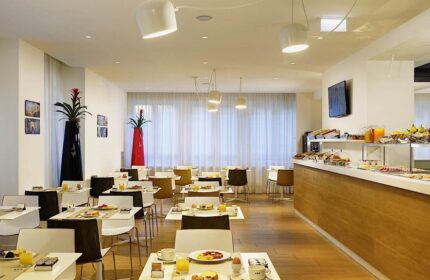 UNAHOTELS Century Milano breakfast area. Gay-friendly hotel with buffet, tables set with juice, coffee, and pastries. Modern, bright interior.