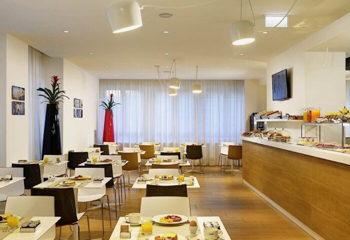UNAHOTELS Century Milano breakfast area. Gay-friendly hotel with buffet, tables set with juice, coffee, and pastries. Modern, bright interior.